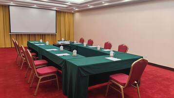 A conference room with a long table, red chairs, a projector screen, and a yellow curtain.