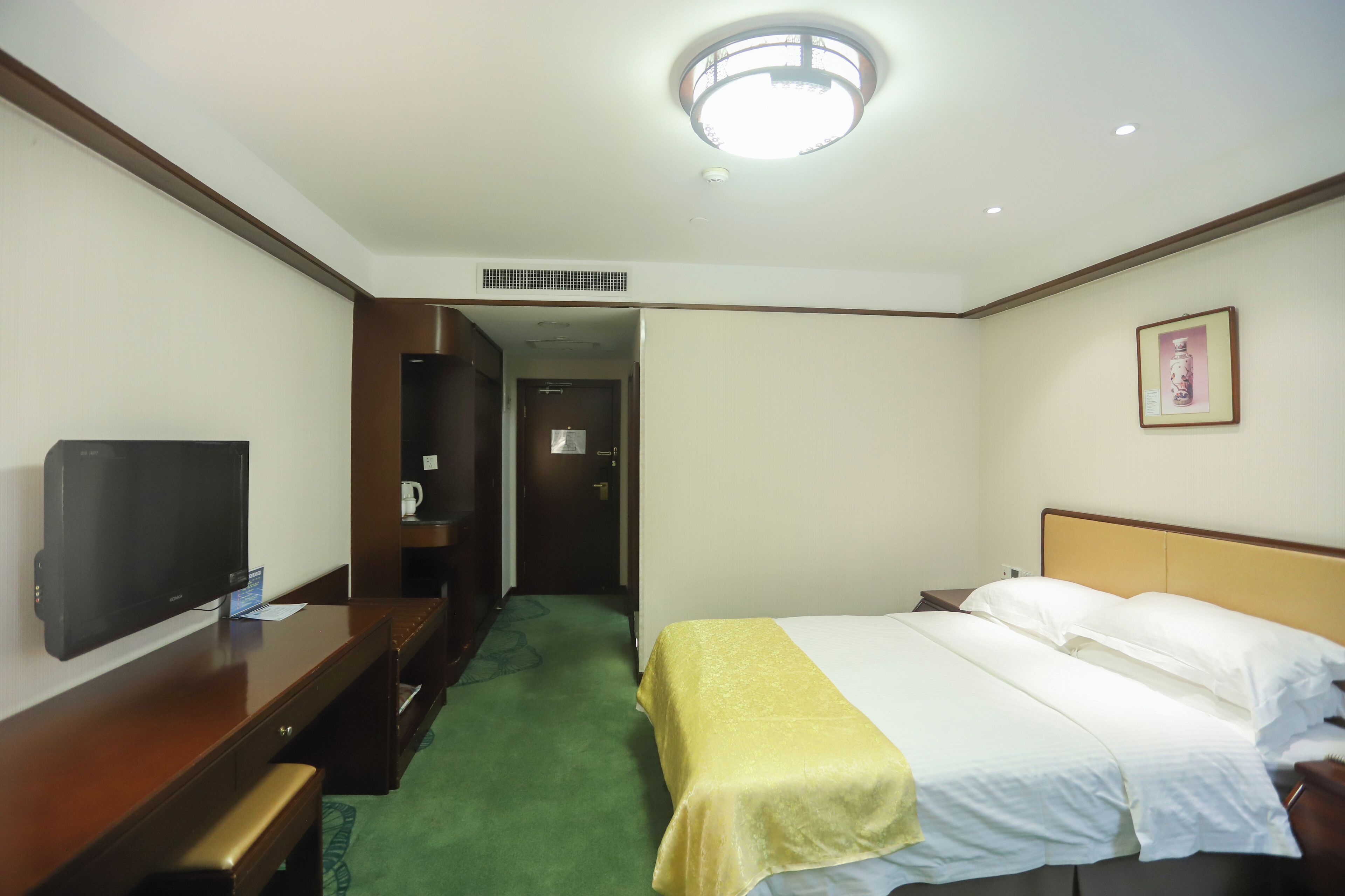 Habitación de hotel con cama, televisor, escritorio y puerta que da a un pasillo.