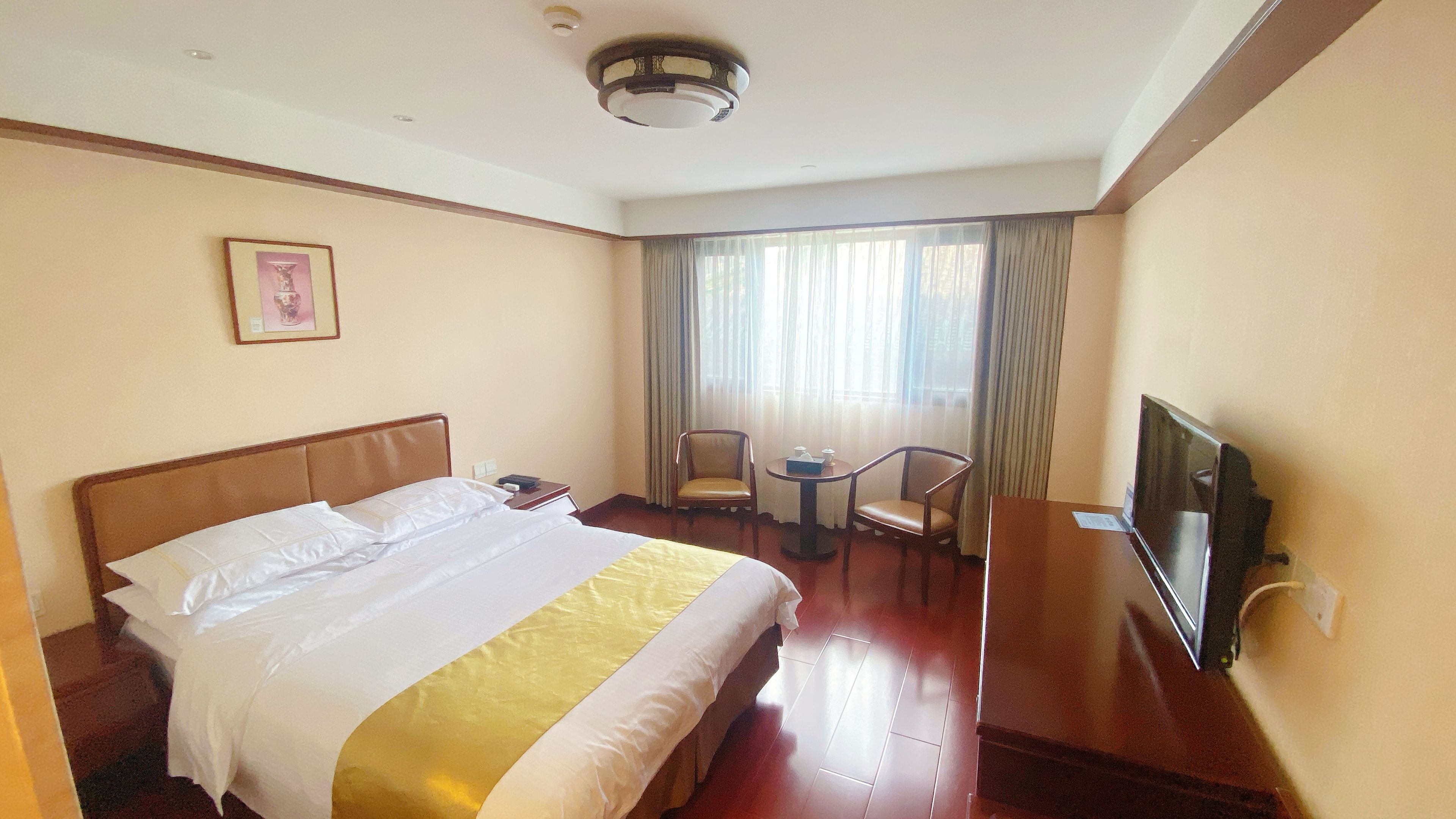 Quarto de hotel com cama, escrivaninha, cadeira, televisão e janela com cortinas.