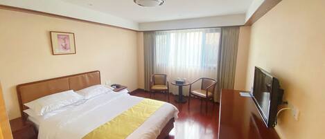 Quarto de hotel com cama, escrivaninha, cadeira, televisão e janela com cortinas.