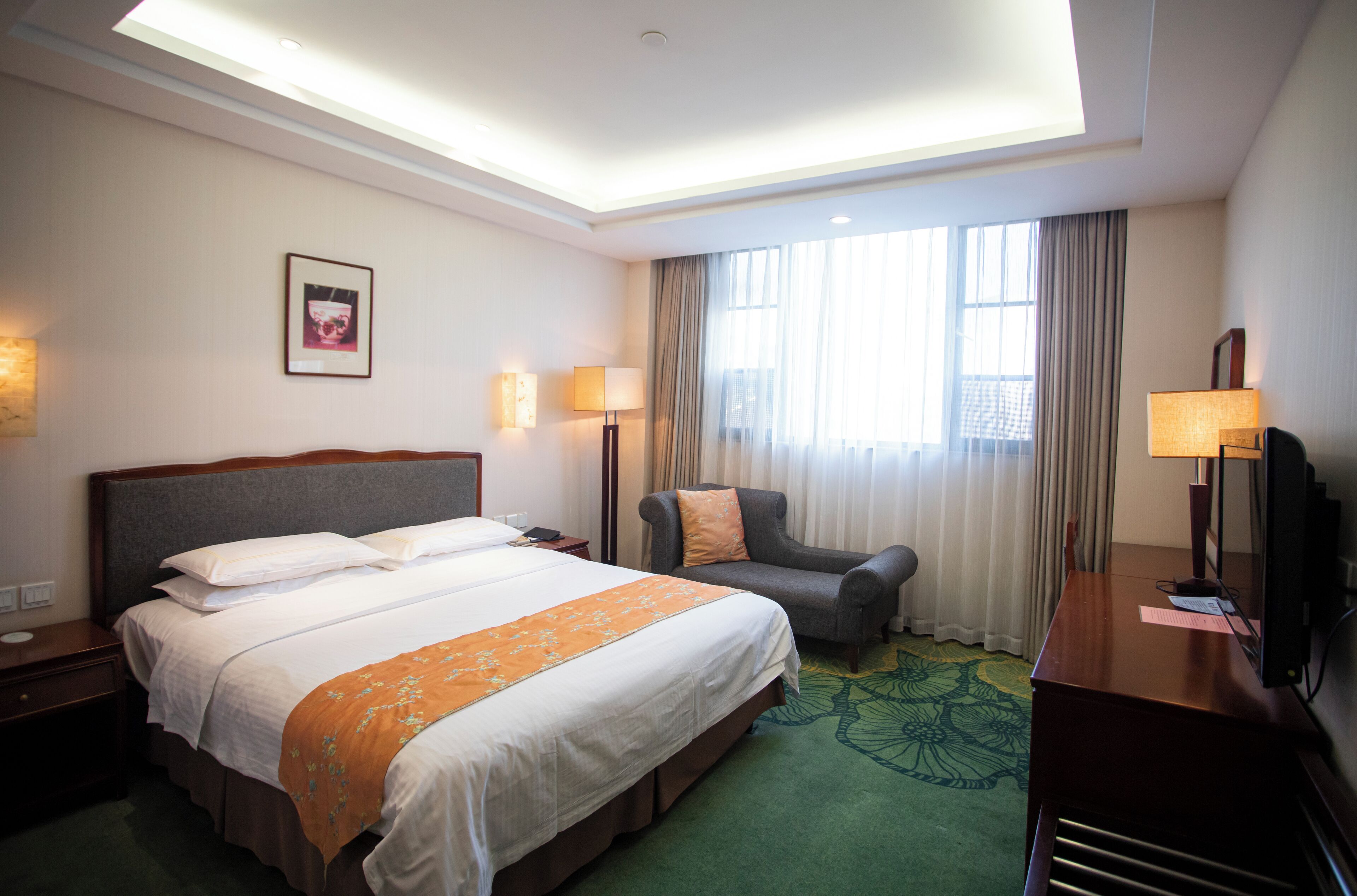 A hotel room with a large bed, a desk with a TV, a chair, and a window with curtains.
