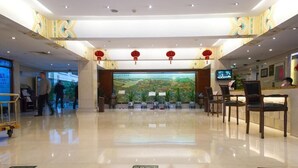 Vestíbulo de hotel con mostrador de recepción, sillas, una pantalla digital grande y un mural decorativo.
