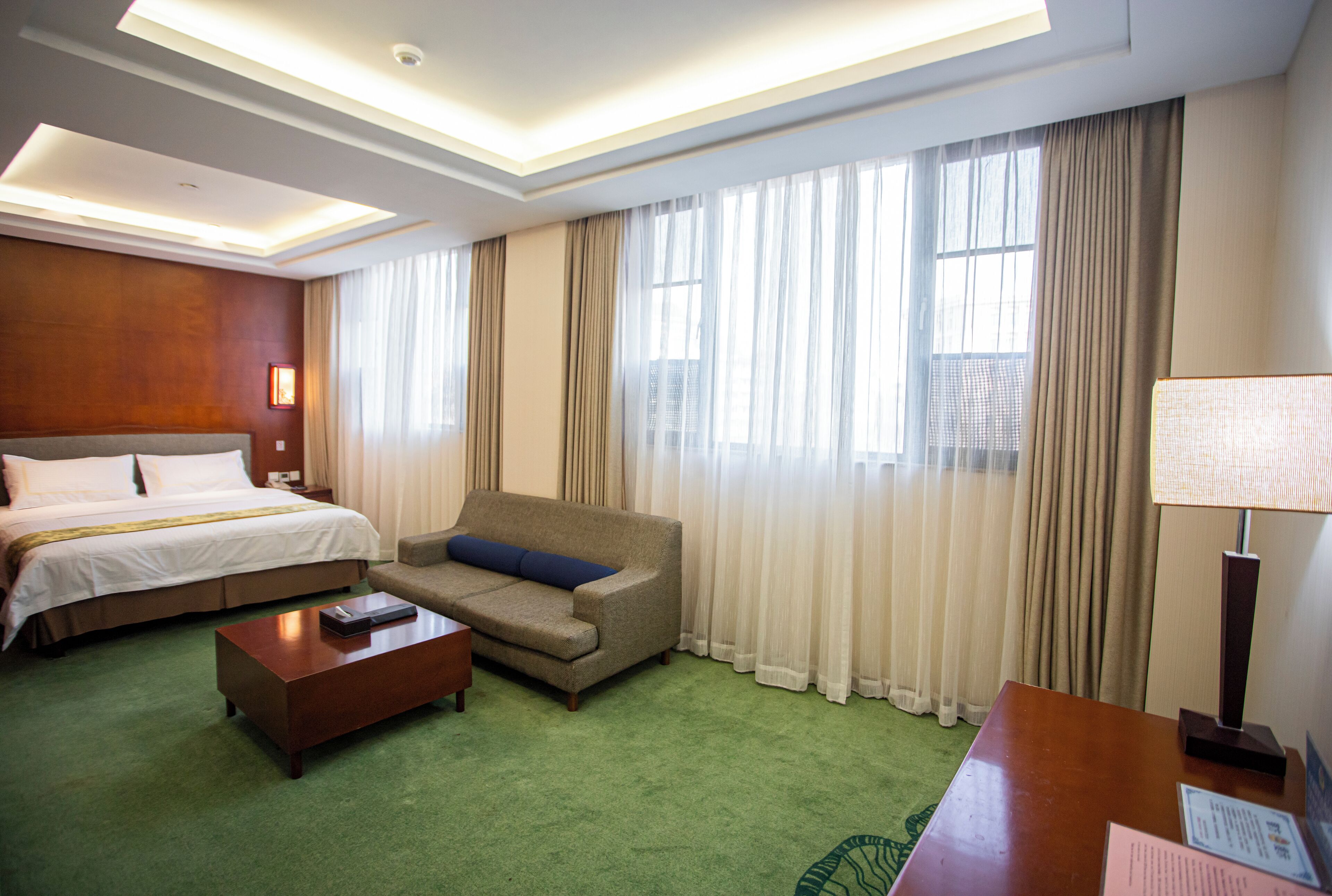 Une chambre d’hôtel avec un lit, un canapé, une table basse et un bureau avec une lampe.