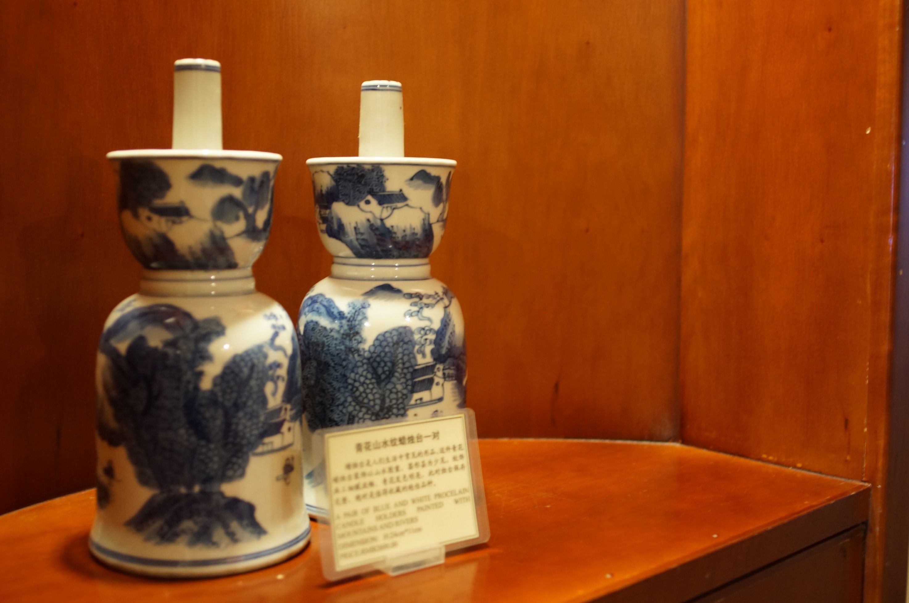 Two ceramic vases with blue and white designs on a wooden shelf.