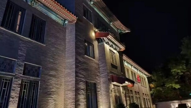 Un edificio tradicional con tejado de tejas y paredes de ladrillo, con varias ventanas y un toldo rojo.