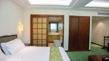 A hotel room with a bed, a wooden wardrobe, a bathroom with a toilet and sink, and a green carpet.