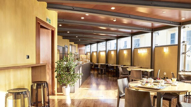 A modern restaurant with wooden flooring, clear glass bar stools, and a potted plant. - B&B HOTEL Imperia Rossini al Teatro (Imperia)