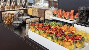 Mostrador de buffet con diferentes opciones de comida, incluyendo frutas, cereales y bebidas.