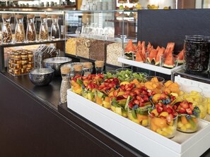Mostrador de buffet con diferentes opciones de comida, incluyendo frutas, cereales y bebidas.