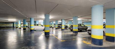 A multi-level underground parking garage with blue and yellow striped pillars, marked parking spaces, and several parked cars.