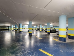 A multi-level underground parking garage with blue and yellow striped pillars, marked parking spaces, and several parked cars. - B&B HOTEL Imperia Rossini al Teatro (Imperia)