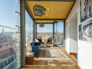 Un apartamento en un edificio alto con un balcón, amoblado con un sofá, sillas y una estatua.