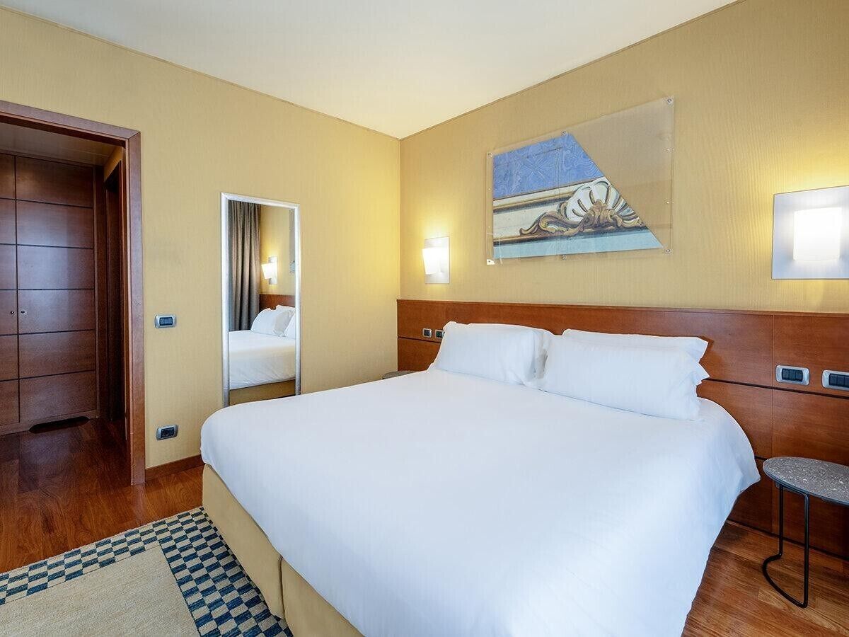 Une chambre d’hôtel avec un grand lit, une tête de lit en bois, un tableau au mur et une petite table.