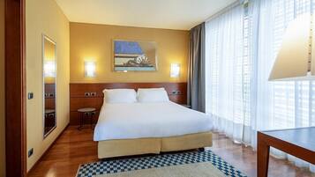 Habitación de hotel con una cama grande, una mesita pequeña, una silla, una lámpara de pared y un cuadro.