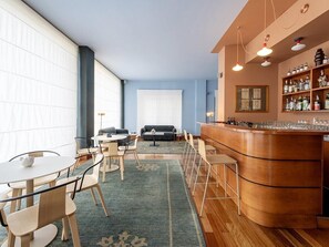 Habitación de hotel con zona de bar, disposición de asientos y un ventanal grande.
