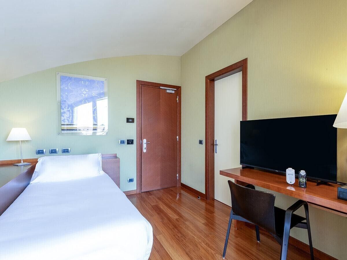 Ein Hotelzimmer mit Bett, Schreibtisch, Fernseher und Fenster.