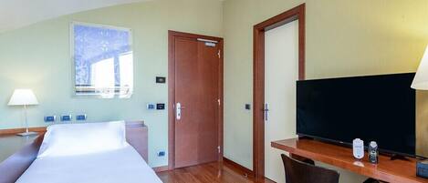 A hotel room with a bed, desk, television, and a window.