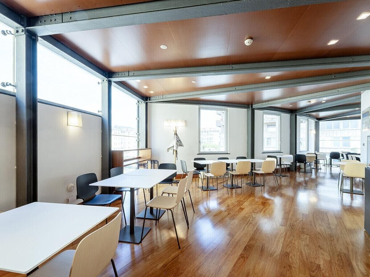 A spacious room with wooden floors, white tables, and chairs arranged for meetings.