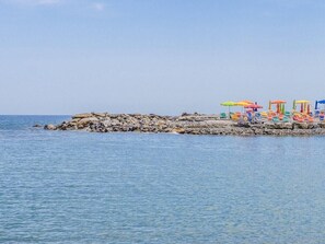 A rocky shoreline with a row of colorful beach umbrellas and chairs. - B&B HOTEL Imperia Rossini al Teatro (Imperia)