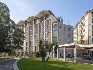Un hotel con fachada moderna, varios balcones y una zona exterior cubierta con bicicletas.