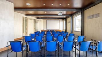 A conference room with rows of blue chairs, a projector screen, and large windows.
