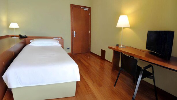 A hotel room with a bed, a desk, a chair, a television, and two lamps. - B&B HOTEL Imperia Rossini al Teatro (Imperia)