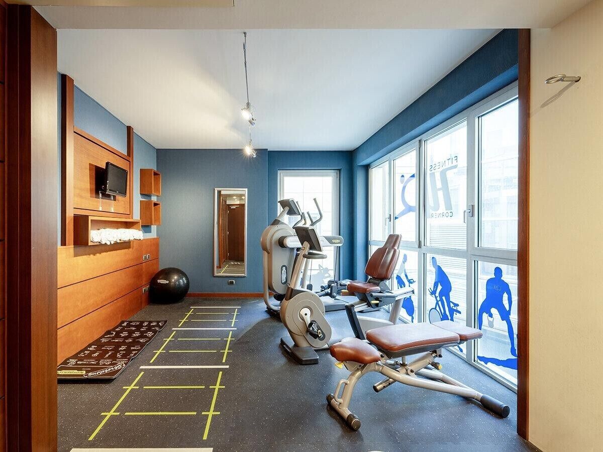 Un gimnasio con equipamiento de ejercicio, un espejo y un ventanal con siluetas de personas ejercitándose.
