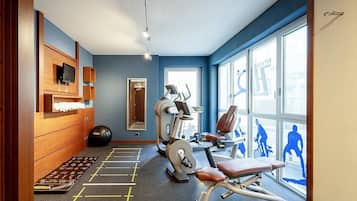 Un gimnasio con equipamiento de ejercicio, un espejo y un ventanal con siluetas de personas ejercitándose.