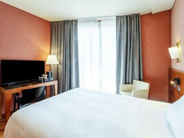 Una habitación de hotel con una cama, un escritorio con televisor, una silla y una lámpara.