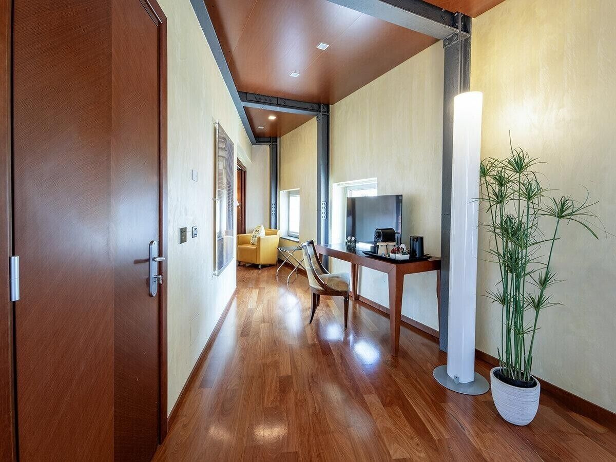 A hallway with wooden flooring, a sofa, a dining table, and a potted plant.