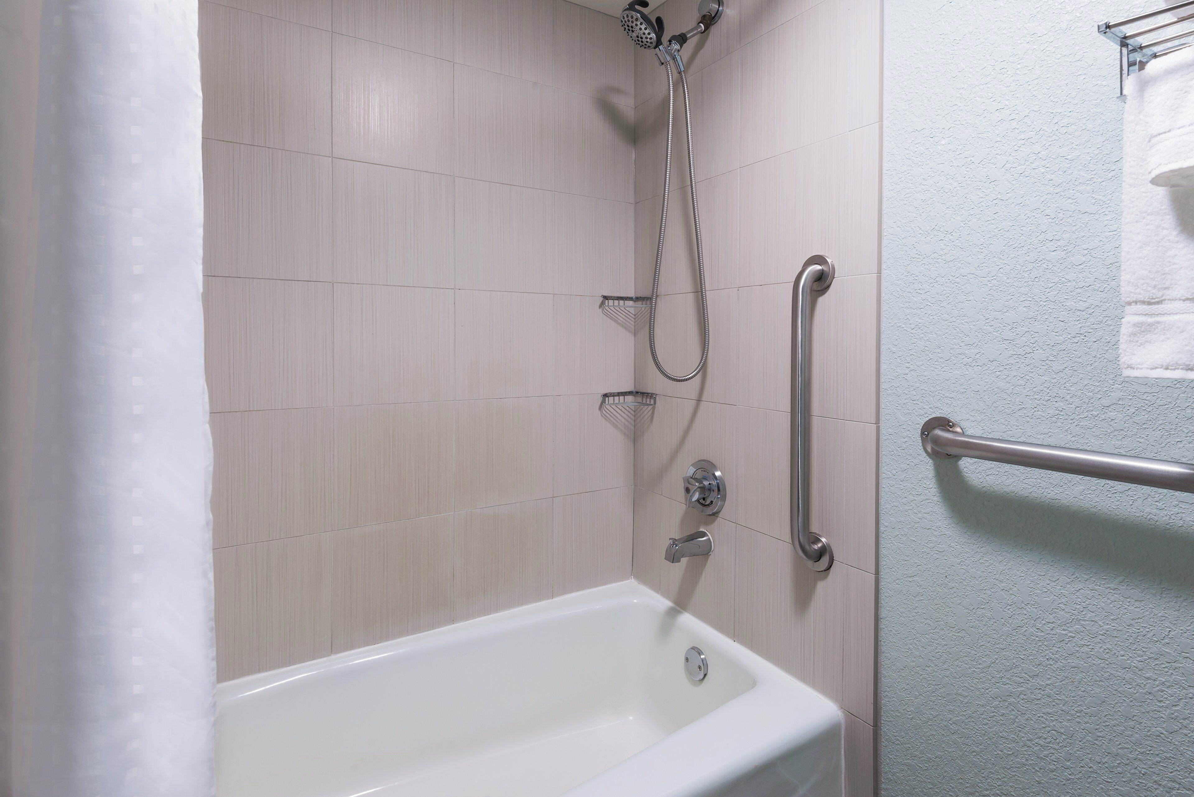 Une salle de bain équipée d’une douche, de barres d’appui et d’une baignoire blanche.