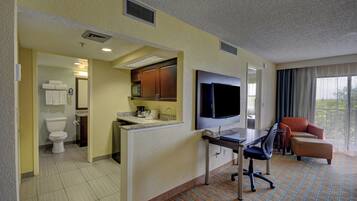 Habitación de hotel con kitchenette, televisor, escritorio, silla y ventana con cortinas.
