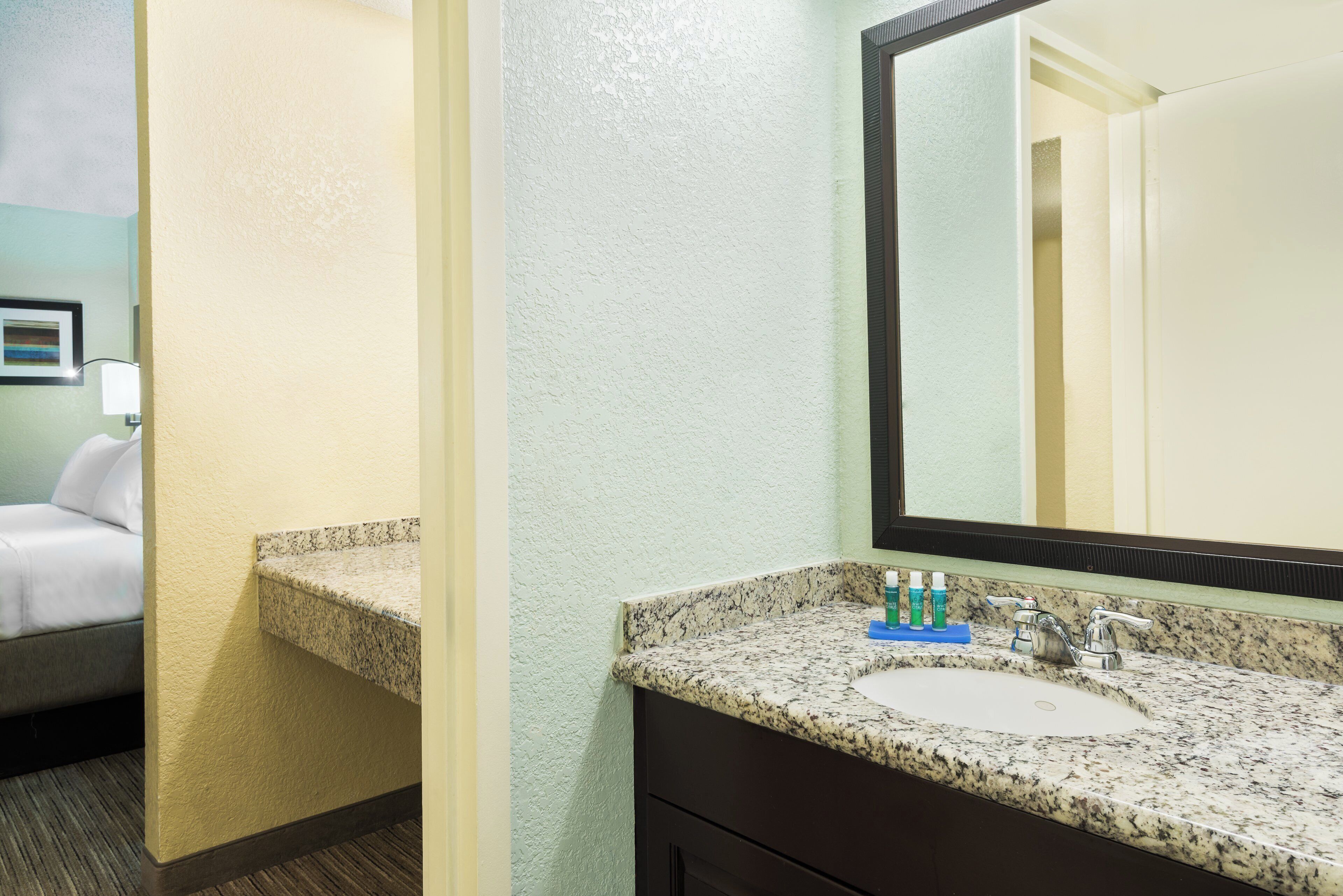 A hotel bathroom with a granite countertop, a sink, a mirror, and toiletries.
