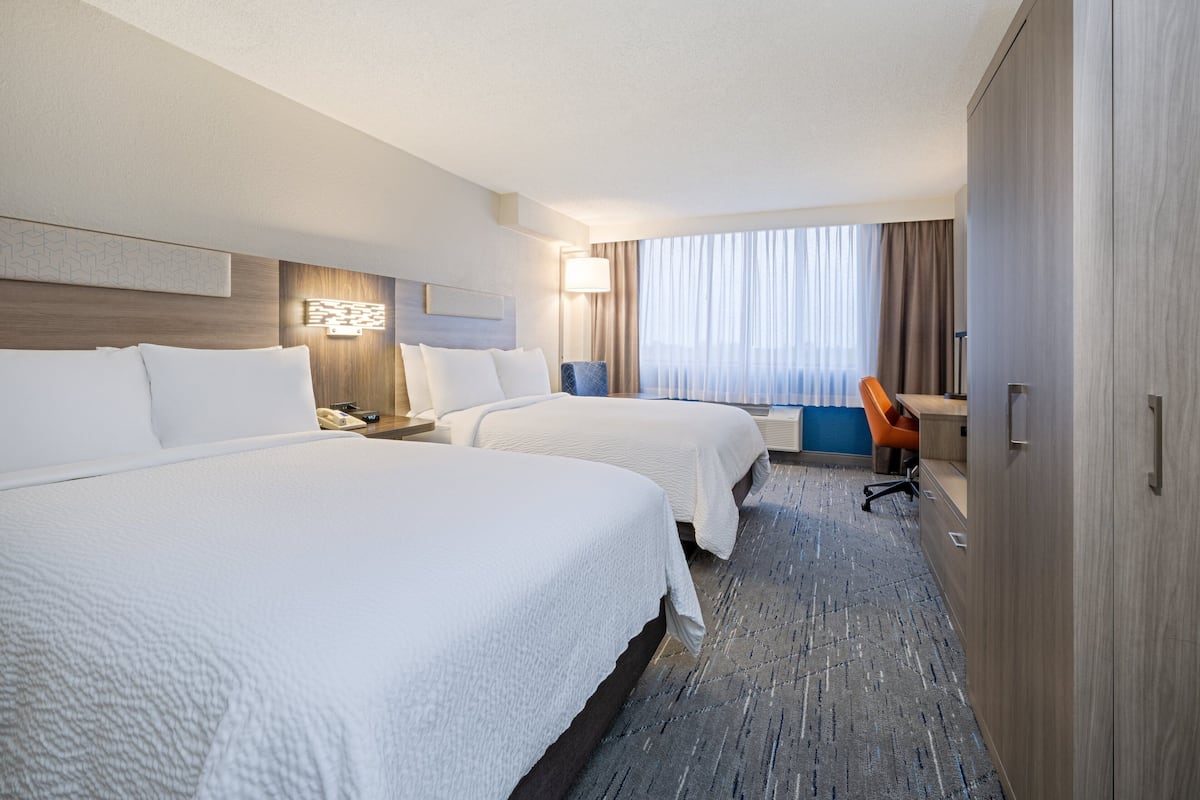 A hotel room with two beds, a desk, and a wardrobe.