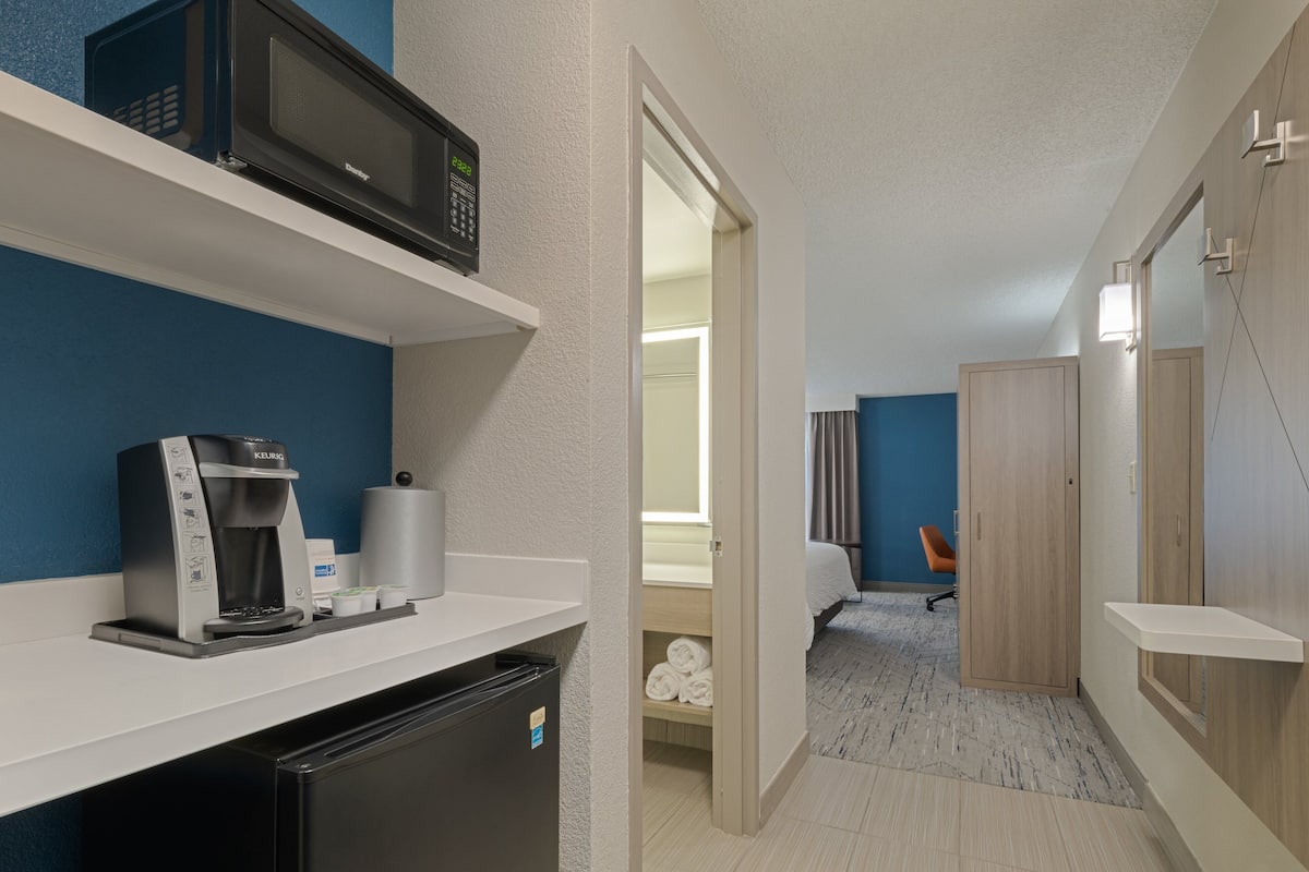 A compact hotel room with a kitchenette, a microwave, a coffee machine, and a small refrigerator.