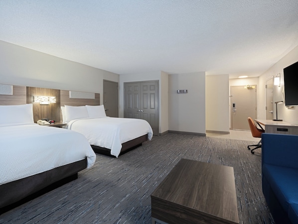 A hotel room with two beds, a desk, a chair, and a television.