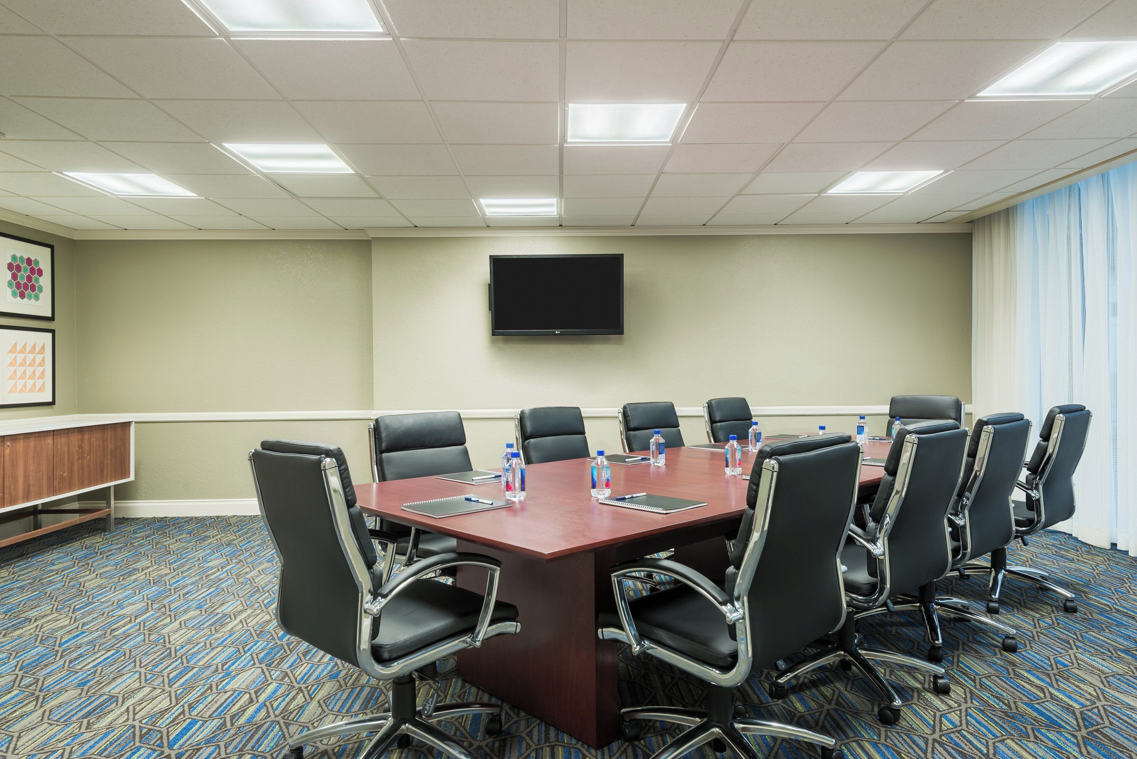 A conference room with a long table, black chairs, water bottles, and a flat-screen TV on the wall.