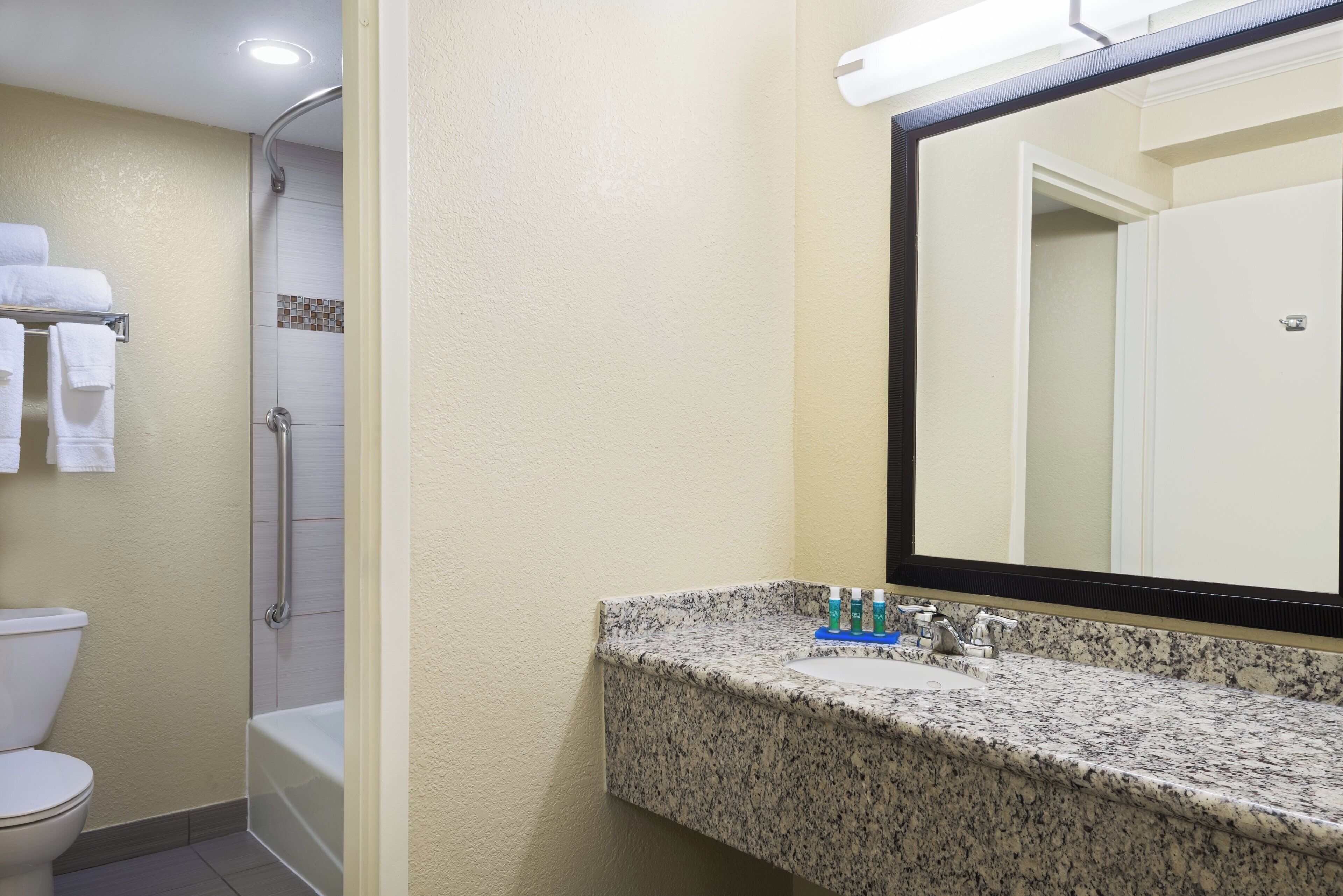 A bathroom with a toilet, shower, and sink with toiletries.