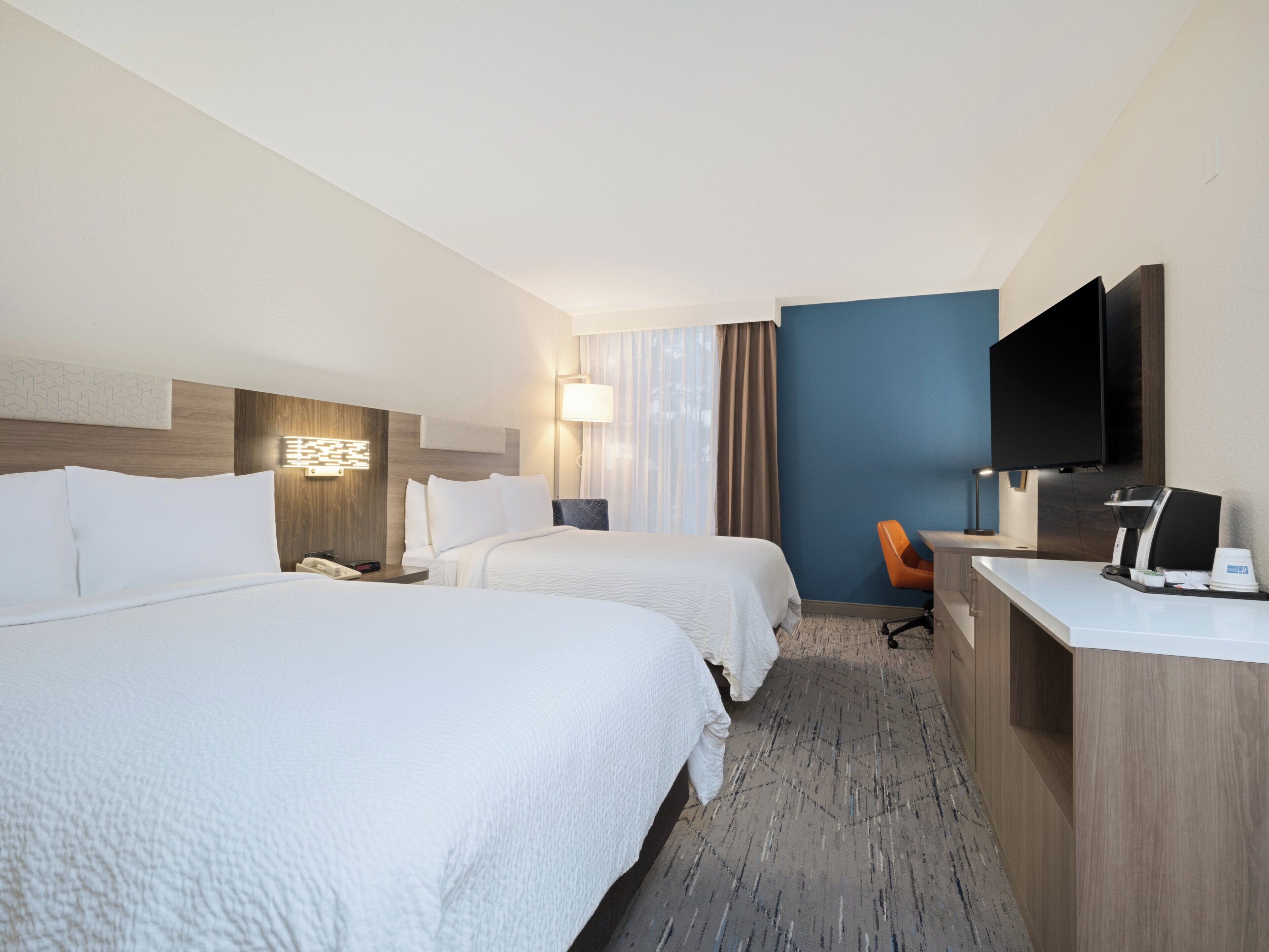 Habitación de hotel con dos camas, un escritorio con cafetera, televisión y lámpara.
