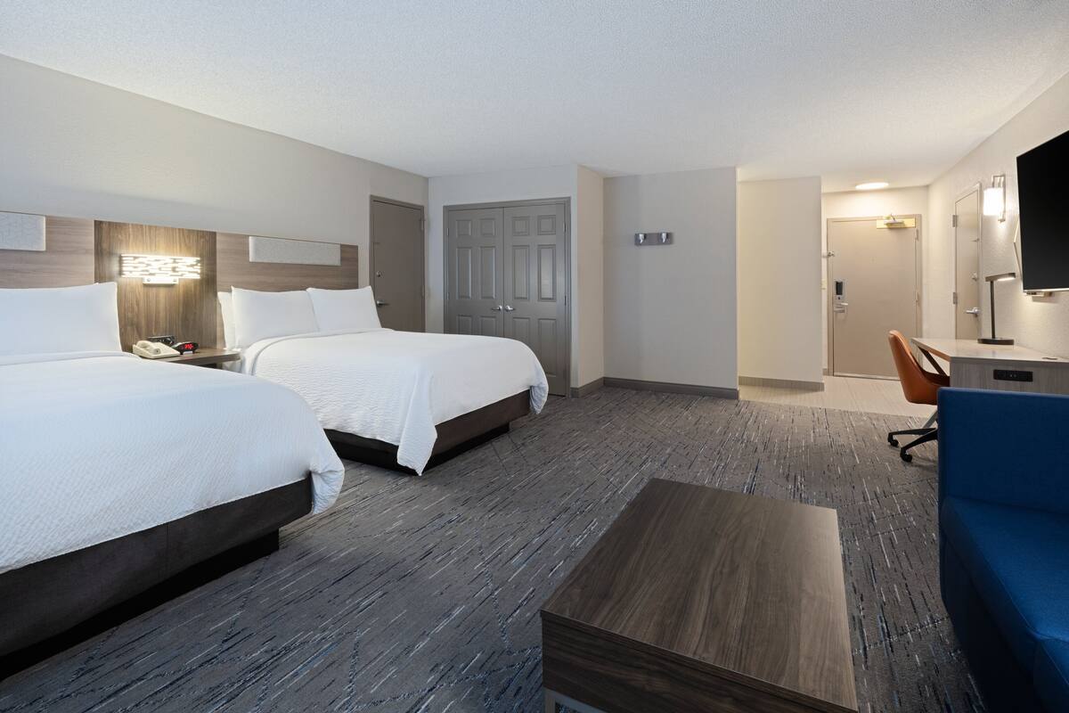 A hotel room with two beds, a desk, a chair, and a television.