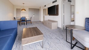 A modern living room with a blue sofa, a wooden coffee table, and a TV mounted on the wall. - Holiday Inn Express Hotel & Suites Ft. Lauderdale-Plantation by IHG (Plantation)