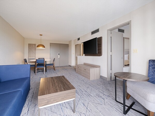 A modern living room with a blue sofa, a wooden coffee table, and a TV mounted on the wall.