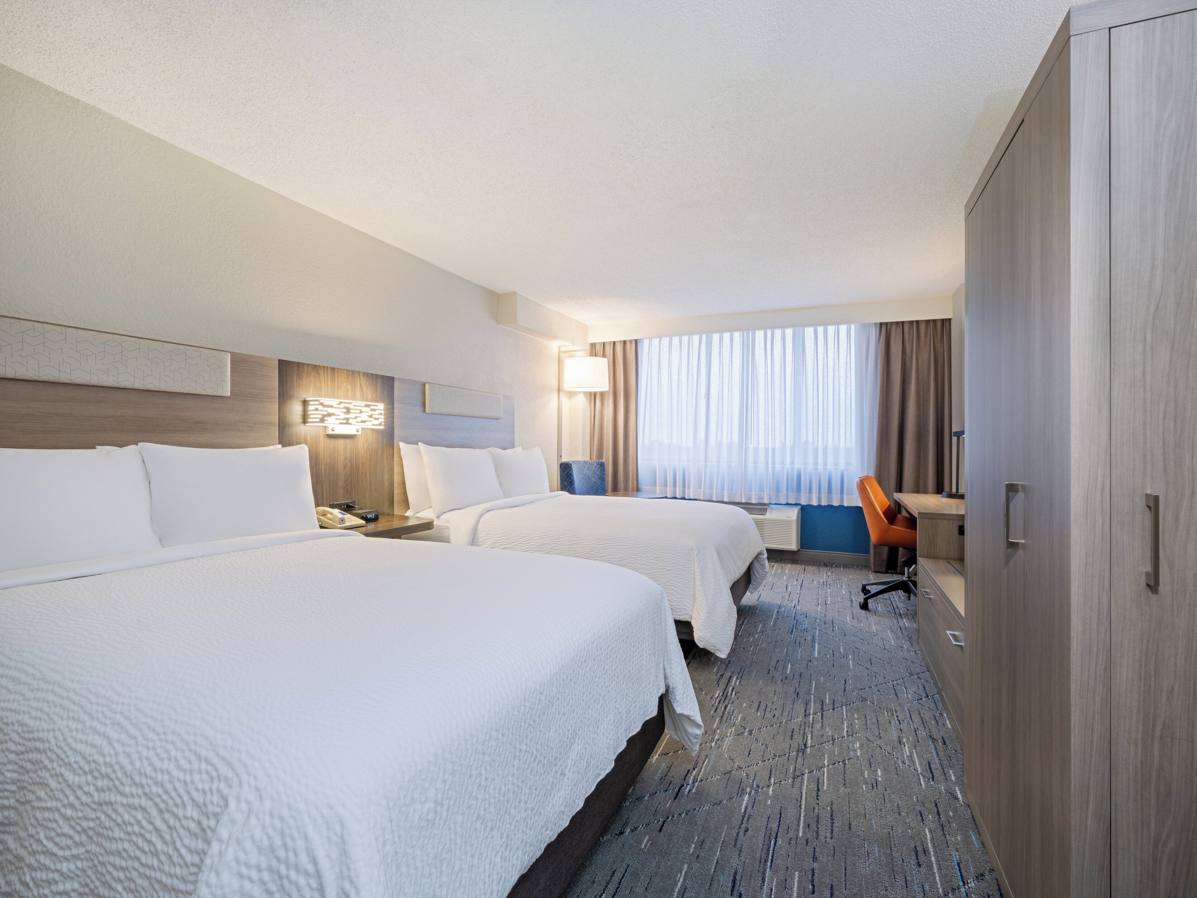 A hotel room with two beds, a desk, and a wardrobe.