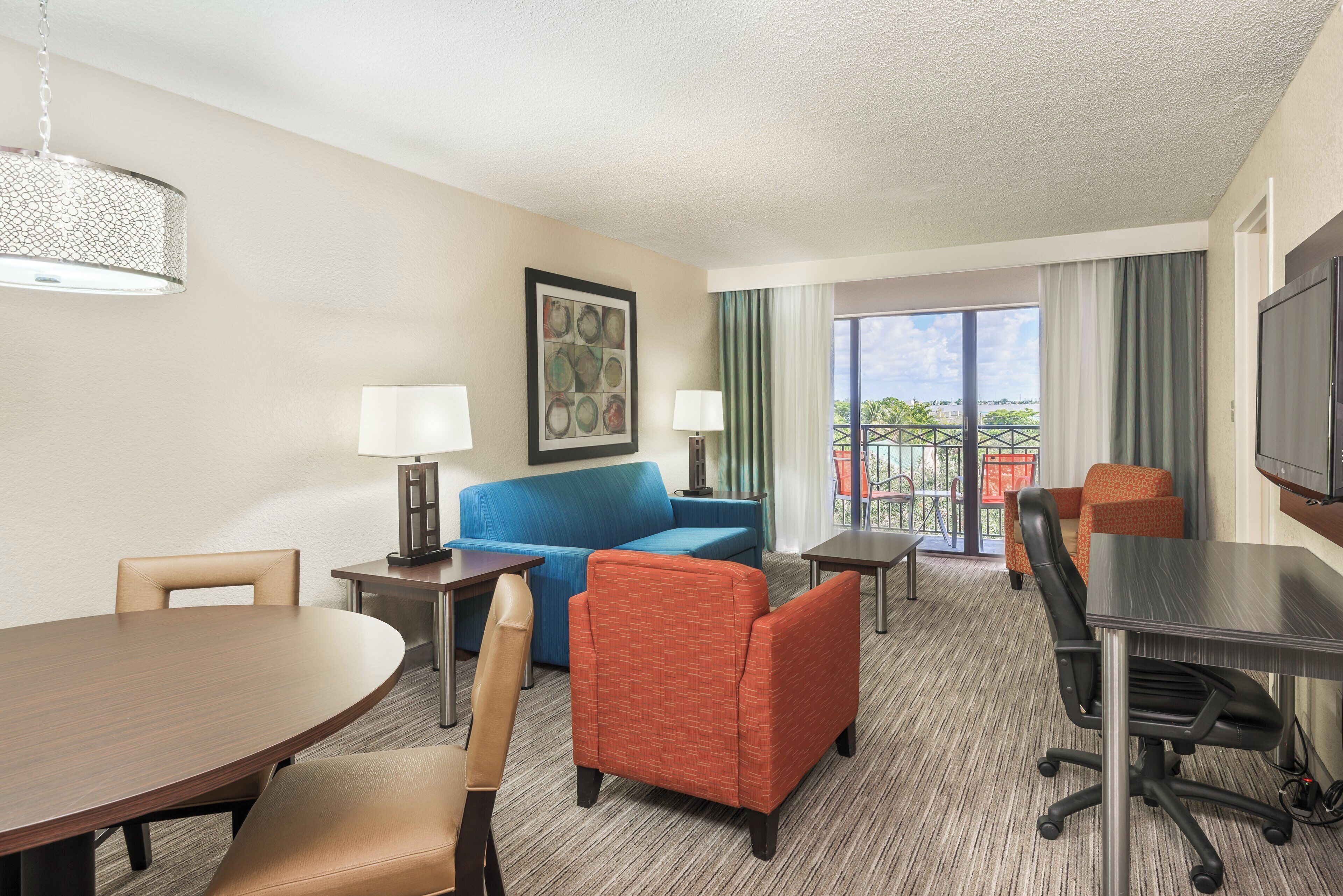 A hotel room with a blue sofa, an orange armchair, a dining table, and a TV.
