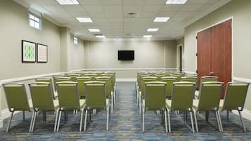 A conference room with rows of chairs, a flat-screen TV on the wall, and a door on the right.