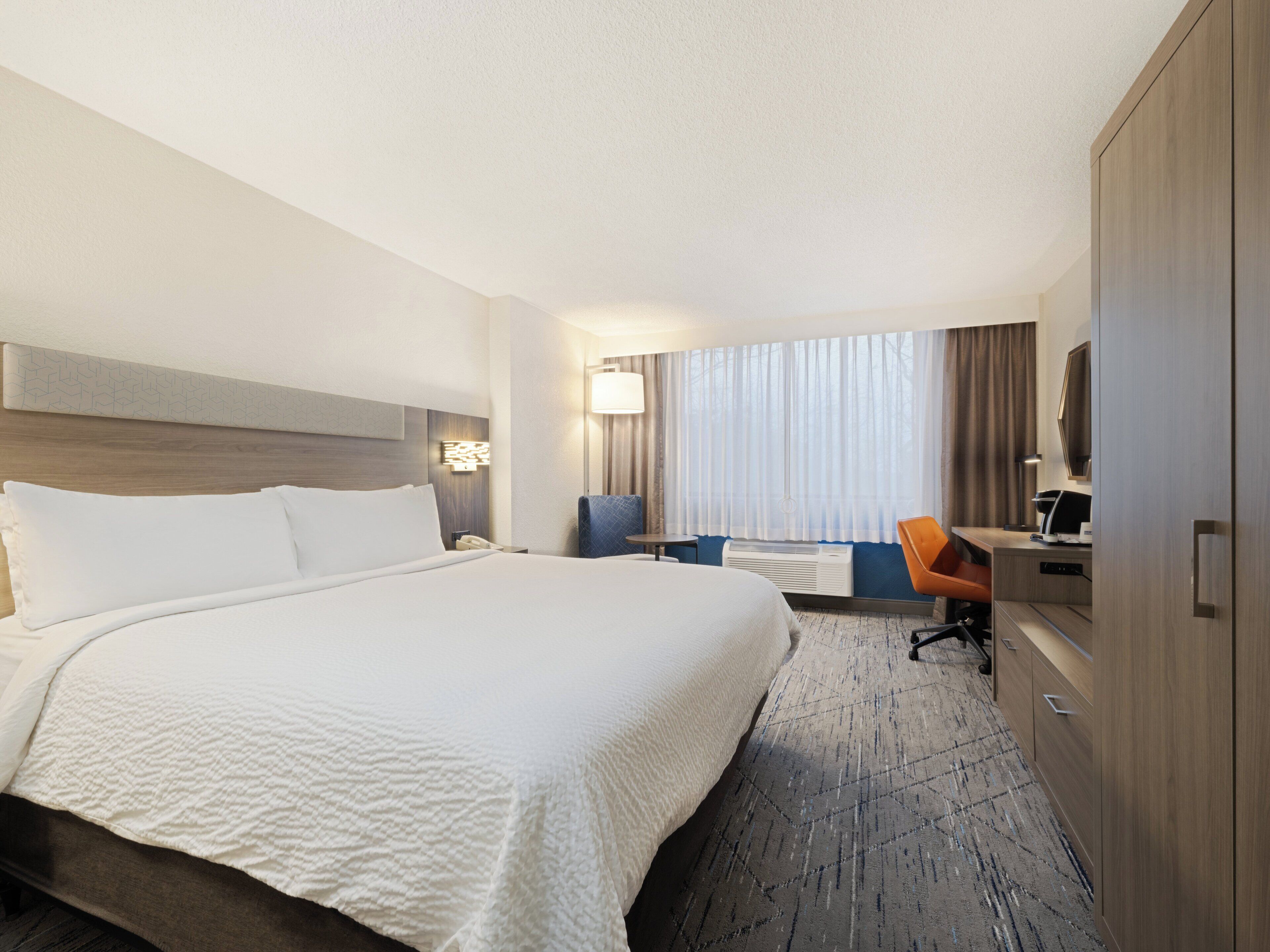A hotel room with a large bed, a desk, a chair, a wardrobe, and a television.