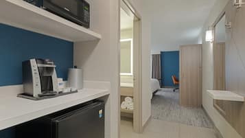 Quarto de hotel pequeno com cozinha compacta, micro-ondas, máquina de café e pequena geladeira.
