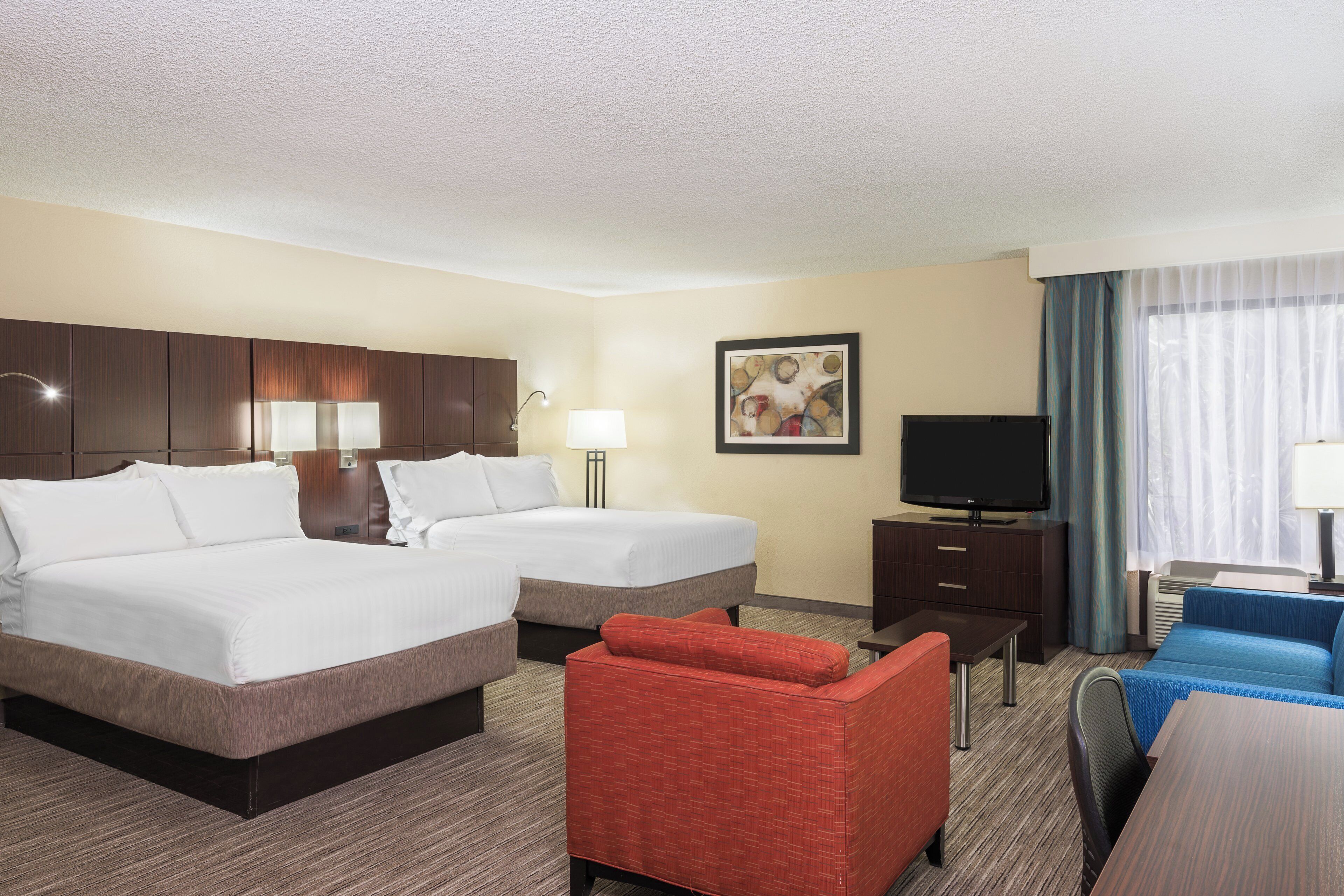 A hotel room with two beds, a TV, a desk, a chair, and a red sofa.