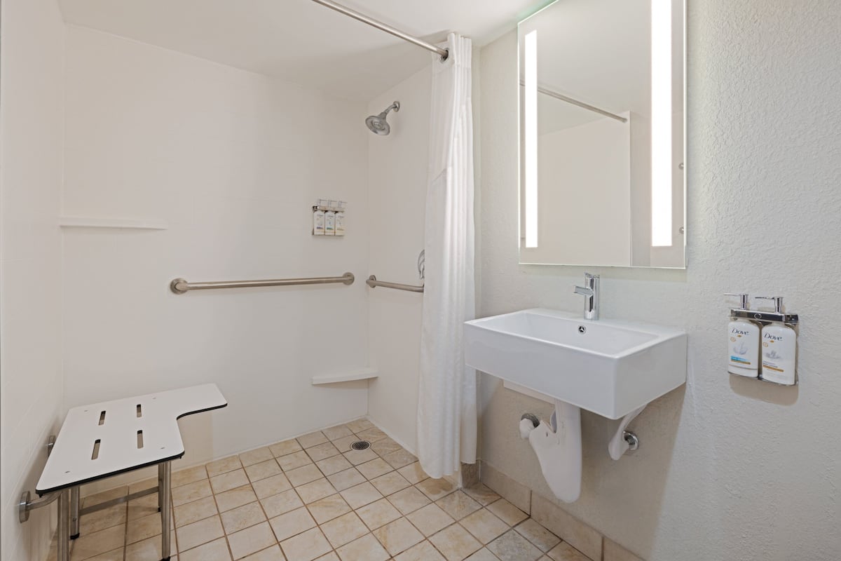 A bathroom with a shower, a sink, and a grab bar.