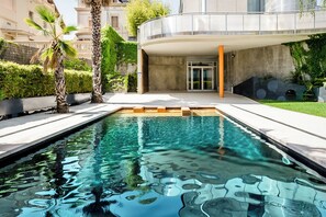 A modern pool area with clear water, surrounded by palm trees and a curved building with a glass entrance. - Ikonik Angli (Barcelona)